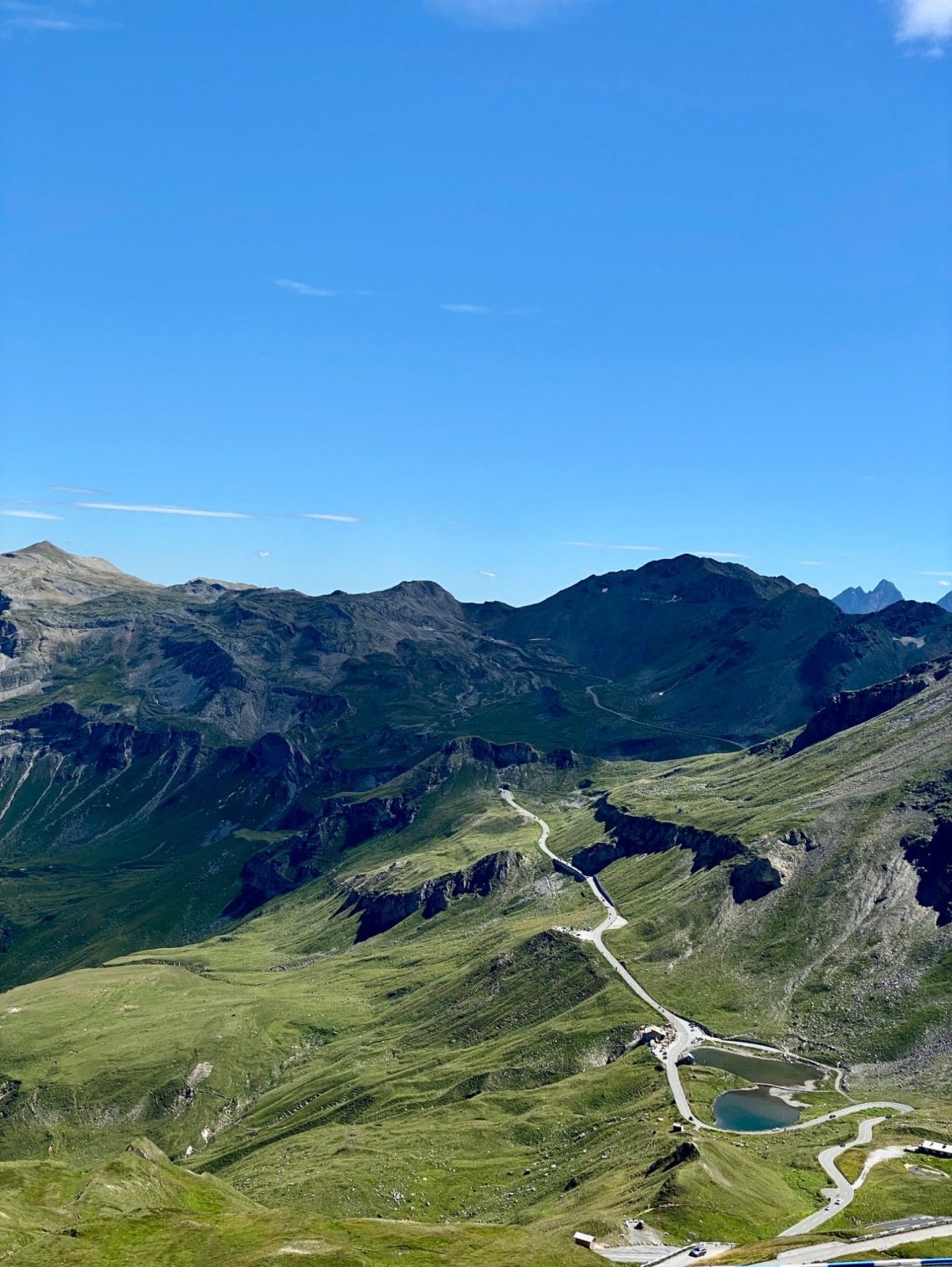 Mann mit Sonnenbrille und Motorradjacke, sitzt im Freien vor grünen Hügeln.