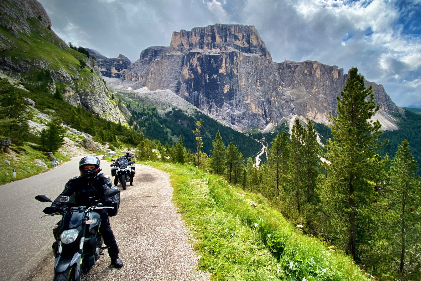 Motorradfahrer auf kurvenreicher Straße, umgeben von Bergen und grüner Natur.
