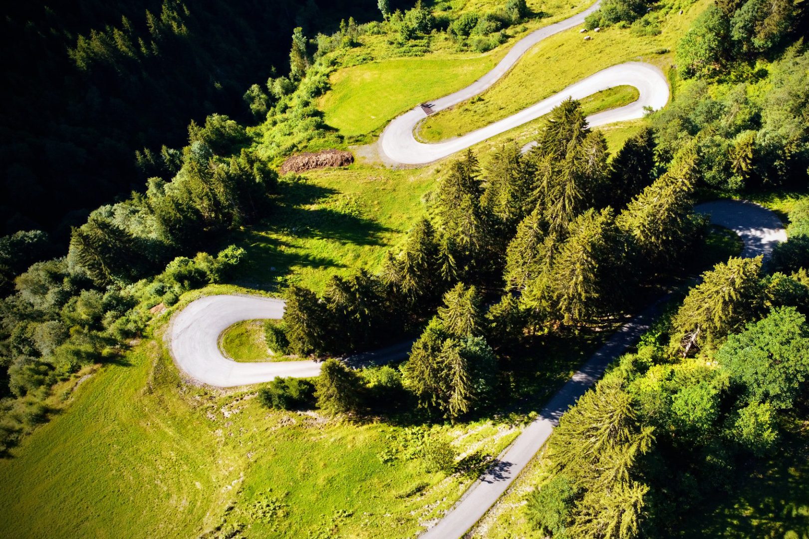 Serpentinenstraße durch grüne Hügel und Wälder in einer bergigen Landschaft.