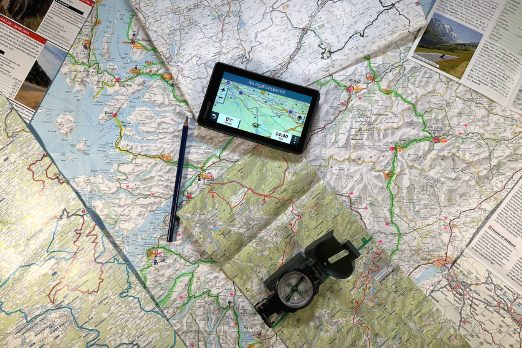 Karten, ein Navigationsgerät und ein Kompass auf einem Tisch, vorbereitet für eine Reise.